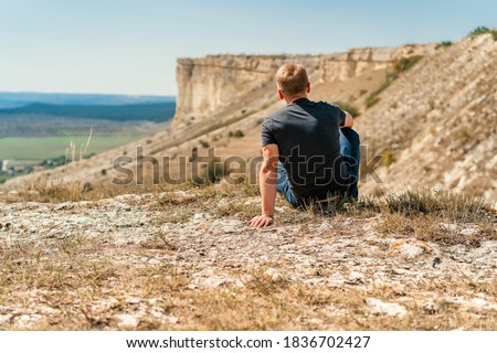 Handsome young blond man sitting on a cliff overlooking the rustic landscape, White rock in Crimea