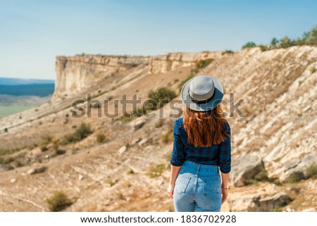 Rear view of a young woman in a plaid shirt and hat standing on a mountain and admiring the landscape, White rock in the Crimea