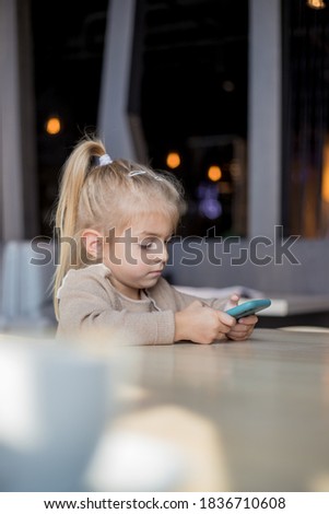 Little cute blonde girl sitting and watching video on mobile phone.