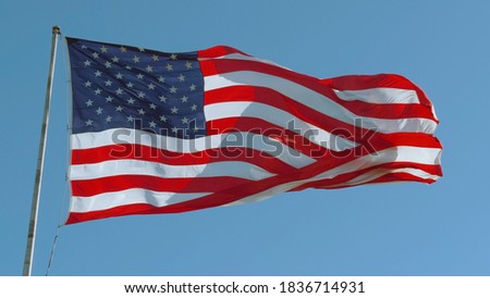 American USA flag on a flagpole waving in the wind against a clear blue sky on a sunny day.