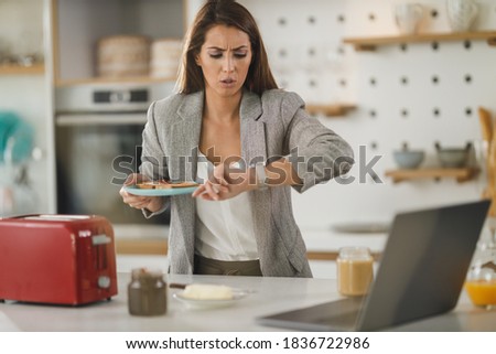 Shot of a stressed multi-tasking young business woman having a breakfast and using laptop in her kitchen while getting ready to go to work. Royalty-Free Stock Photo #1836722986