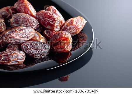 Dried sweet dates on a black plate, black reflective background.