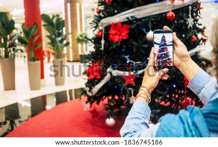 Woman's hands take picture of the beautiful christmas tree in the shopping mall - concept of holidays and consumerism
