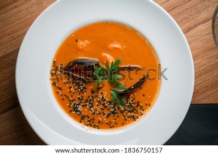 Gourmet serving of spicy tomato soup with fried mussels and chili peppers on a plate and wooden table isolated. Delicious seafood mussels . Lemon and baguette . Clams in the shells. Top view.