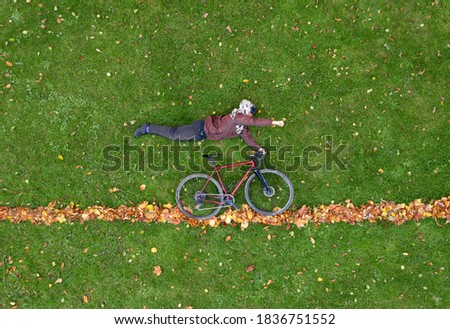 Young lies on the green lawn in a superman pose with a bicycle. Creative trendy autumn concept. Drone top view.