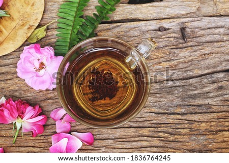 Hot tea and pink rose on wood background