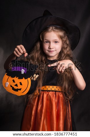 Halloween kids. Portrait of a cute little girl wearing a witch dress and hat on a dark background.