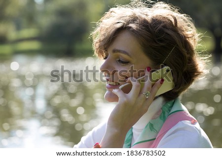 Young woman in the park speaks by mobile phone. Cute girl portrait in french style.