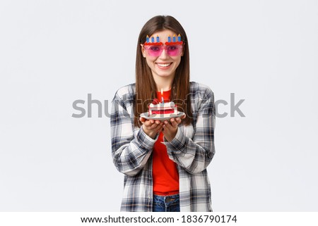 People lifestyle, holidays and celebration, emotions concept. Cheerful cute girl in glasses holding birthday cake, celebrate b-day, making wish to blow lit candle, white background