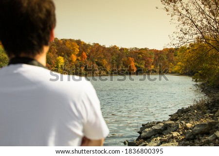 A beautiful and colorful autumn landscape around the lake in golden sunset time, blur foreground of young man in casual white t-shirt enjoy a view