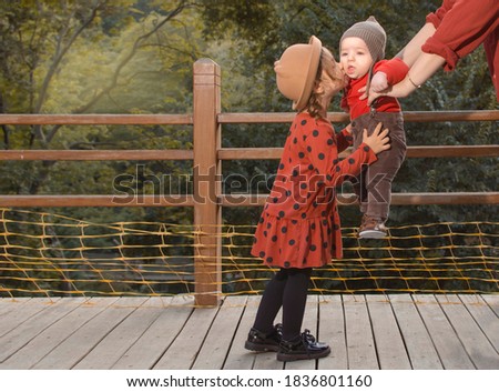 Outdoor portrait of cute cheerful little girl in hat and brown polka dot dress kissing her small baby brother. Sunset time. Happy family. Cheerful kids outside in fall time. Autumn colors picture.