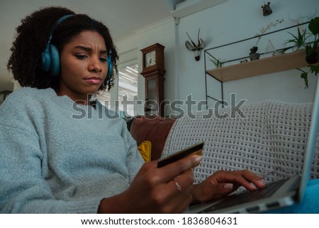 Mixed race female frowning while making online payment using laptop sitting on sofa in trendy lounge.