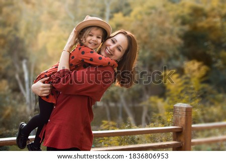 Outdoor portrait of cute cheerful little girl in hat and brown polka dot dress with her mother. Sunset time. Happy family. Cheerful kid outside in fall time. Autumn colors picture. Mommy and daughter.
