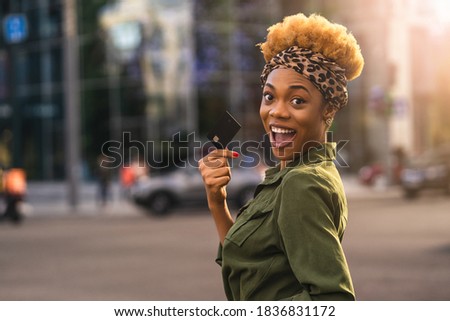 Happy Afro American beautiful woman walking on the street while holding debit card. Shopping concept. Copy space