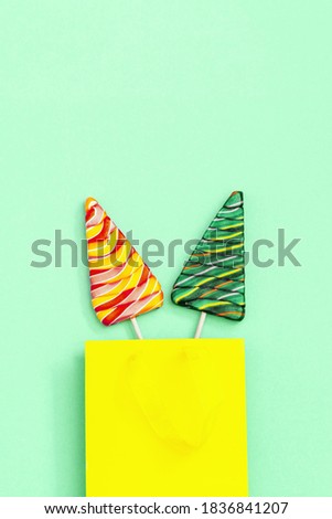 Lollipops shaped like Christmas tree. Creative  New Year Flat lay with sweet candy lollypops with stripes on stick in paper bag on neo mint colored background.