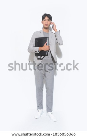  full length young man in wearing gray suit with gray sweater with gray pants and sneakers shoes holding purse  uses a smartphone