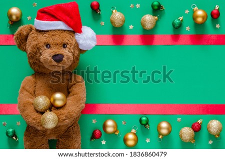 Smiling teddy bear holding Christmas baubles on blurred green background with ornaments. Christmas and New year concept.