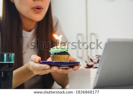 Young Asian woman is holding a birthday cake to wish her friend over a video call by a tablet during the coronavirus to keep social distance.