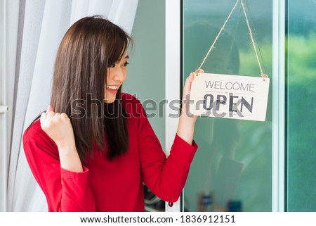 Asian young woman glad and smiling she notice sign wood board label "WELCOME OPEN" hanging through glass door front shop, Business turning open after coronavirus pandemic disease, back to new normal