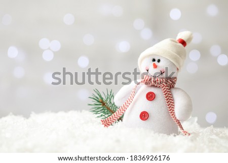 Snowman toy and branch of fir tree on snow against blurred festive lights, space for text. Christmas decoration
