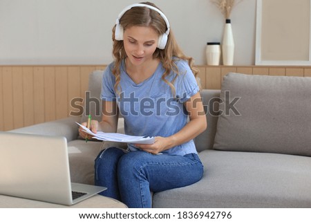 Smiling girl sit near couch watching webinar on laptop. Happy young woman study on online distant course.