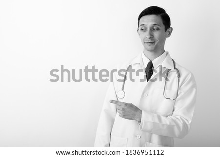 Studio shot of young handsome man doctor pointing to the side against white background