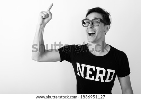 Studio shot of young happy nerd man smiling while thinking and pointing finger up against white background