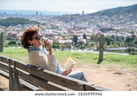 A woman having a coffee and with a notebook, in a mountain viewpoint with views of the city