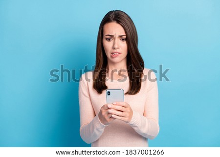 Photo of nervous girl use smartphone feel fear bite lips teeth wear pastel jumper isolated on blue color background