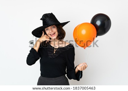 Young witch holding black and orange air balloons making phone gesture. Call me back sign
