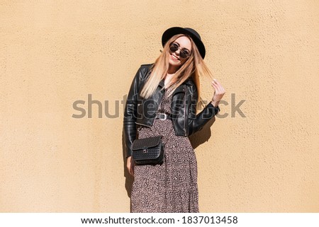Happy fashion woman with autumn trendy outfit in stylish leather jacket and dress with black small bag