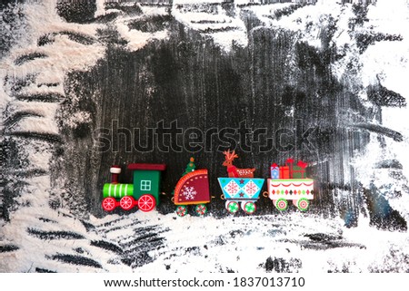 A toy wooden train carries gifts and Christmas paraphernalia on a dark, snow-covered background. Image for a decorative Christmas holiday concept. Winter frame. Free space for copying
