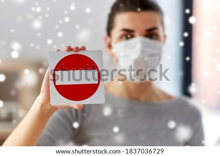 health, safety and pandemic concept - young woman in protective medical mask showing stop sign at home in winter over snow