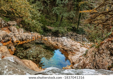 Mountain canyon and rocks in the autumn forest with floating leaves and reflections of the sky in the water of fonts and backwaters.