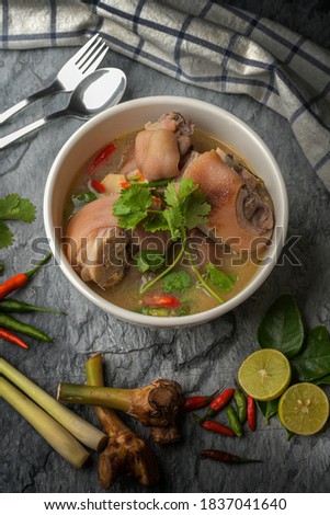 Tom Yum Pork Leg with Spicy Thai Style Soup Pasted on a dark gray stone pattern background.