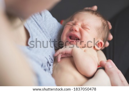Portrait of a newborn 2 weeks old in the hands of parents. The boy is crying. Colic in the tummy. Pregnancy, motherhood, preparation and expectation of motherhood, the concept of child birth. Royalty-Free Stock Photo #1837050478