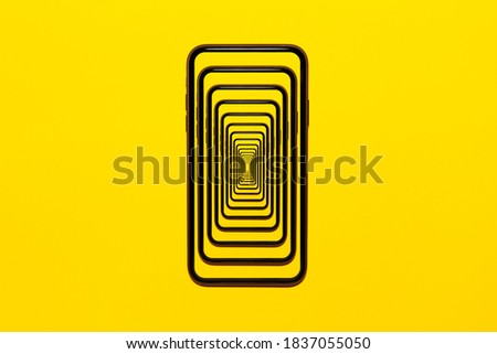 Enigmatic surrealistic optical illusion. Close-up modern smartphone isolated on yellow background.