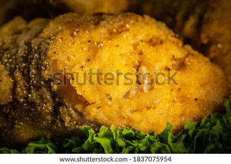 Cod fish fried in corn flour in a black plate on the black background.