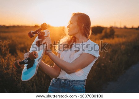 girl with a longboard skateboard in her hands on the background of the sunset