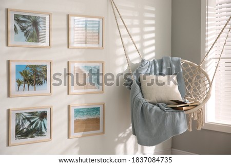 Different pictures on wall and hanging chair in room. Artworks in interior design