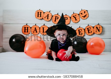 beautiful baby girl in witch halloween costume at home, sitting on bed with Halloween decoration, Lifestyle indoors