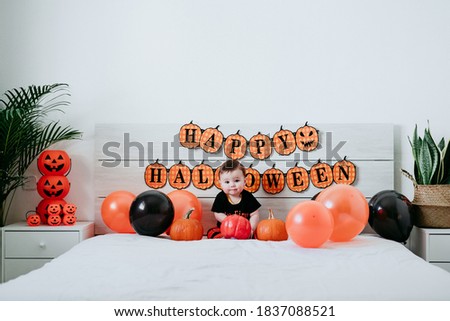 beautiful baby girl in halloween costume at home, sitting on bed with Halloween decoration, Lifestyle indoors