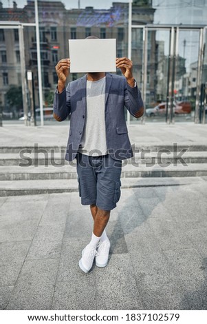 Stylish dark-skinned male person crossing legs while standing on the foreground