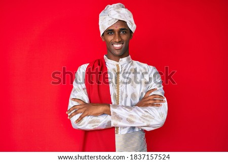 Handsome indian man wearing tradition sherwani saree clothes happy face smiling with crossed arms looking at the camera. positive person. 