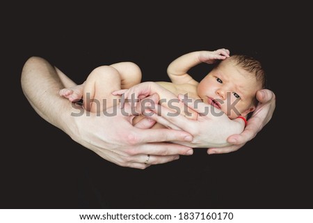 Portrait of a newborn baby boy 2 weeks old in the hands of his parents on a black background. Pregnancy, motherhood, preparation and expectation of motherhood, the concept of child birth.