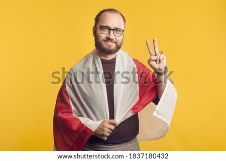 Closeup portrait of a Belorussian man in studio with a national white red white flag and victory sign. Protest and revolutionary concept against Lukashenko. Minsk, Belarus Royalty-Free Stock Photo #1837180432