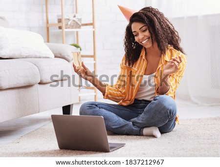 Virtual Party. Happy african american woman in hat having video conference online meeting with friends and family, holding glass of wine, toasting and celebrating birthday, staying at home Royalty-Free Stock Photo #1837212967