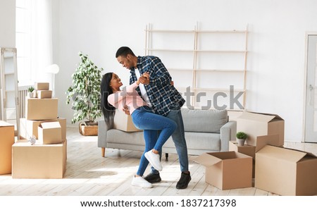 Loving black couple dancing in their house among carton boxes on moving day. Happy young African American family having fun while relocating to new property. Panorama