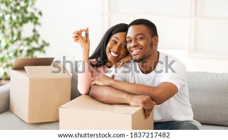 Happy black couple with house key and carton boxes looking at camera and smiling in their property, panorama. Young African American homeowners excited to move into new apartment Royalty-Free Stock Photo #1837217482