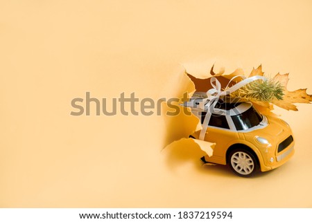 toy car bursts through torn paper, autumn on yellow paper. The concept of a cozy and modern autumn. Trend yellow background, copy space